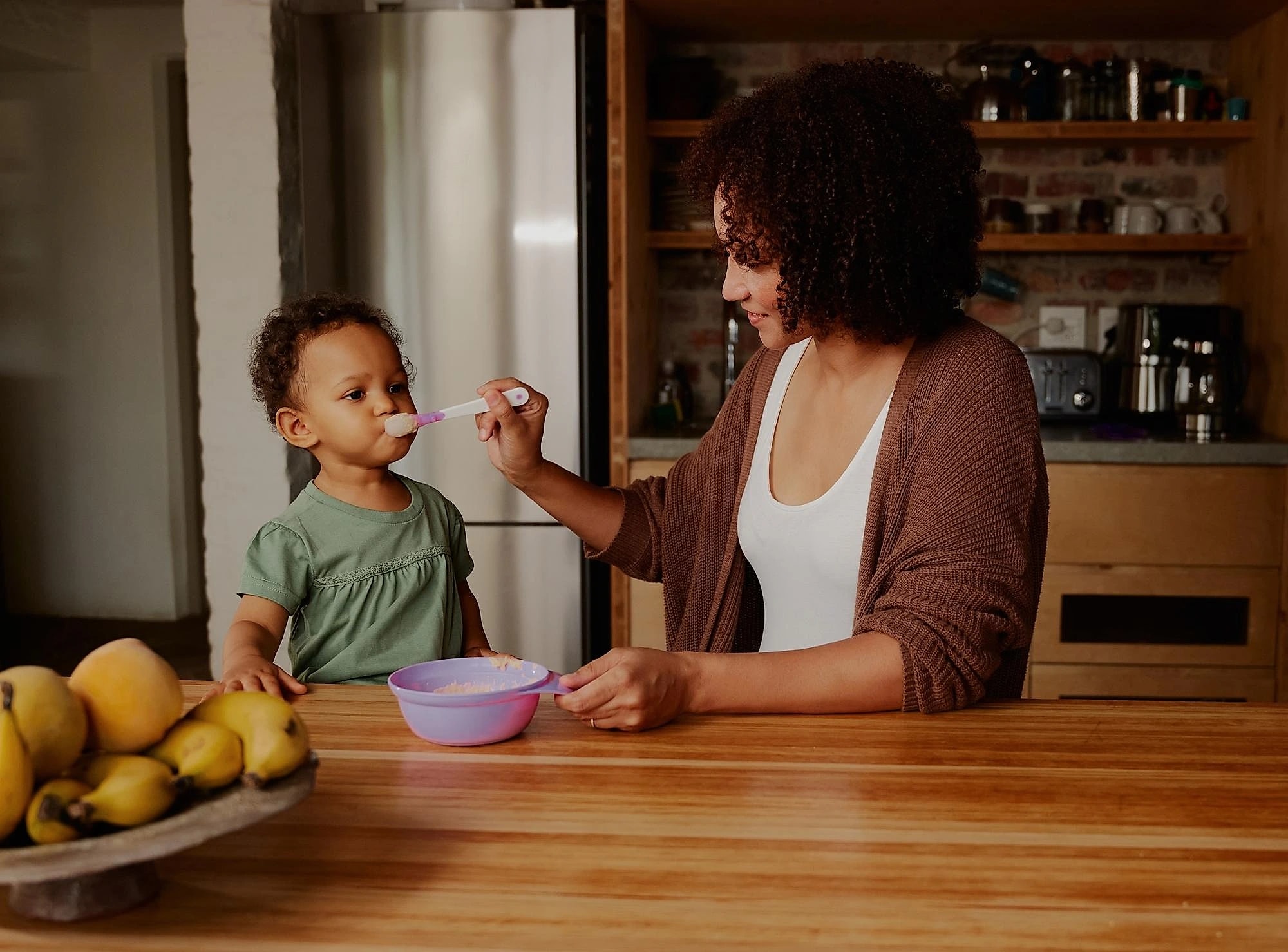 Mãe dando comida ao filho pequeno na cozinha de casa